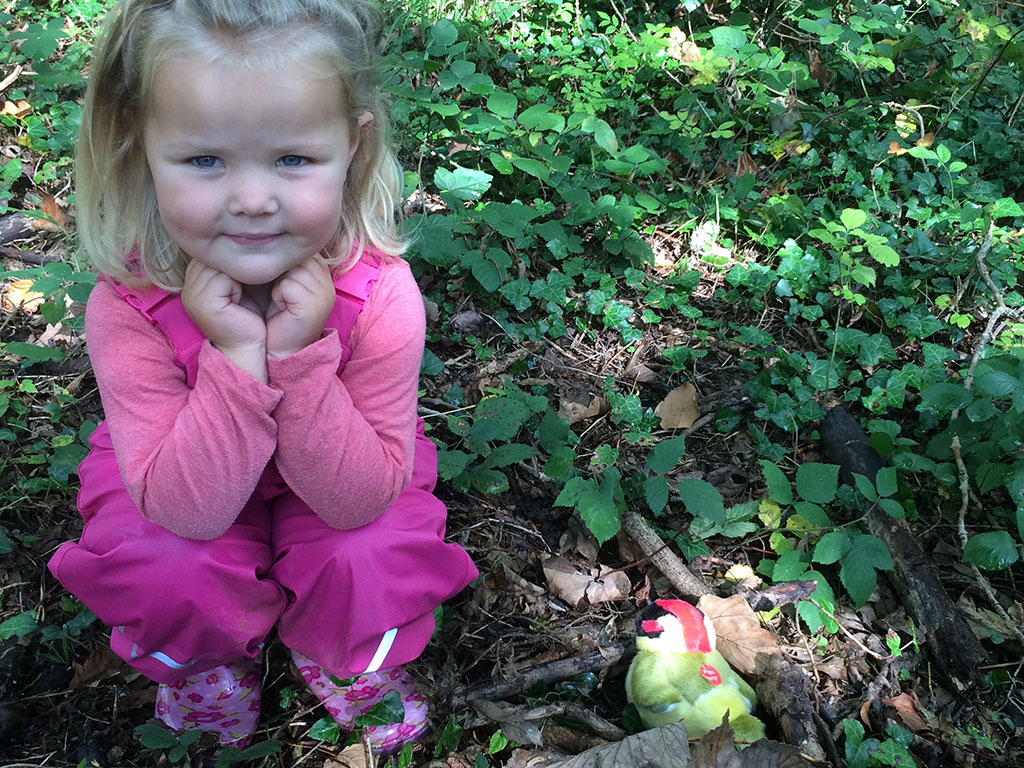 little girl crouching on forest floor