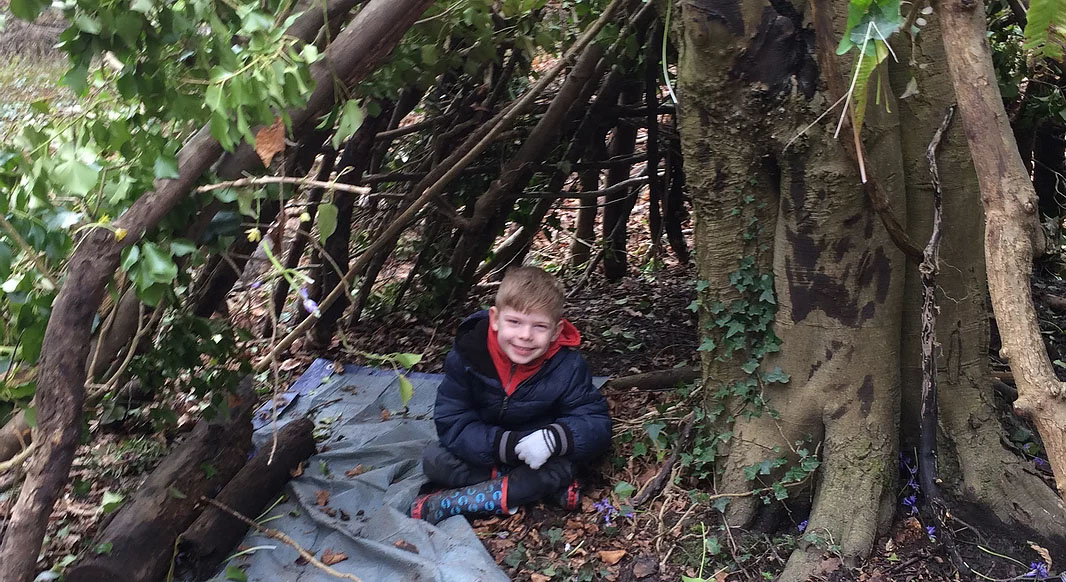 child sitting under a structure constructed with branches